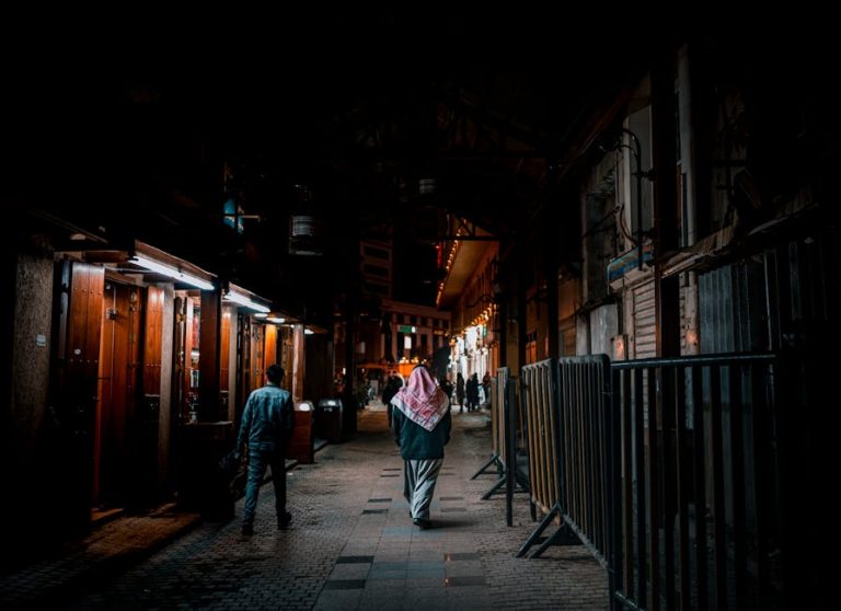 A nighttime scene in a bustling market alleyway in Kuwait City with traditional architecture and people.