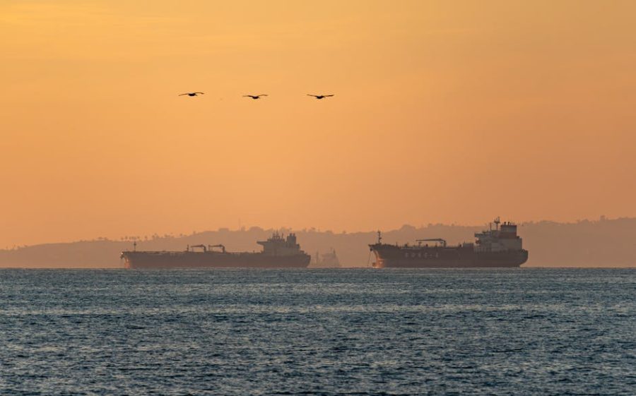 Silhouetted oil tankers on the Pacific Ocean at sunset near Long Beach, California.